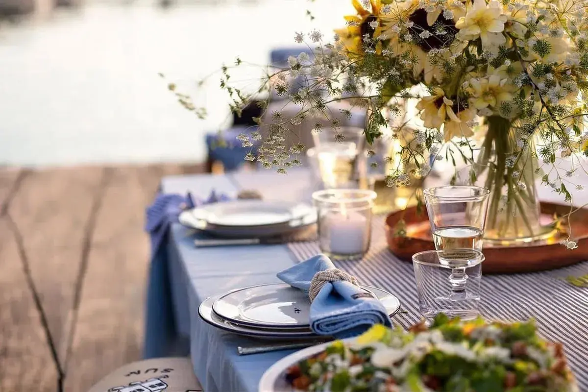 Vacker dukning vid vattnet för ett somrigt mat midsommar. Blommor, ljus och tallrikar redo för fest.