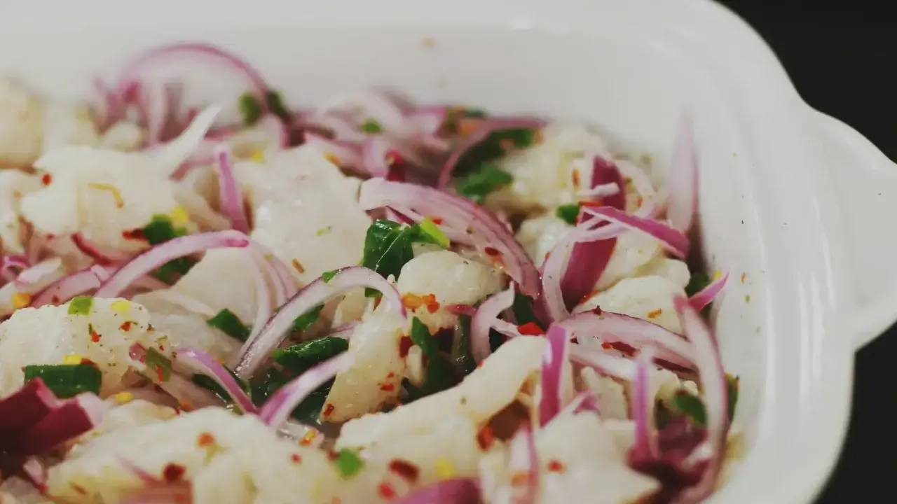 En närbild på en skål med färsk ceviche, med bitar av vit fisk, rödlök, chili och örter. Perfekt för ett somrigt ceviche recept.
