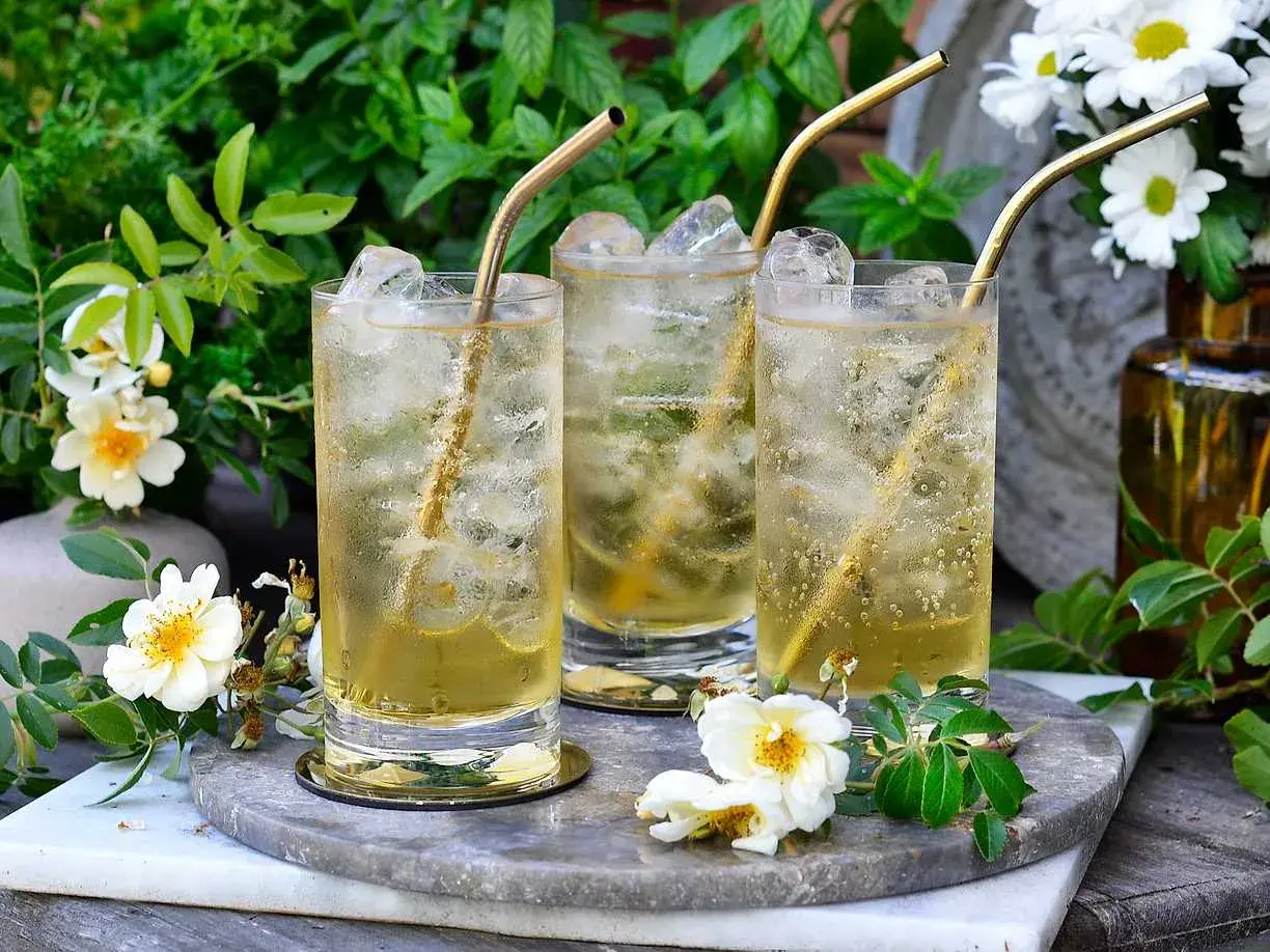 Tre glas med is och gyllene sugrör. En uppfriskande geting drink i en lummig trädgård.