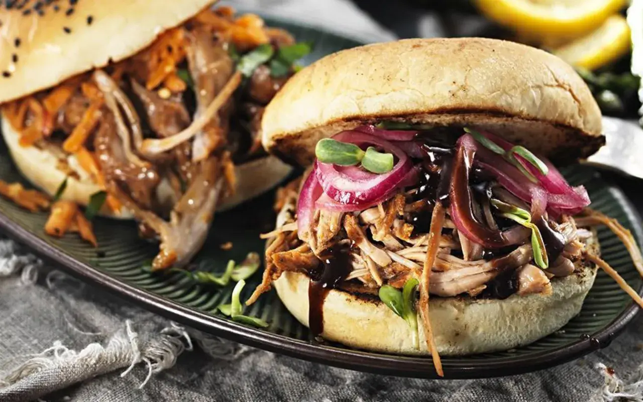 Två saftiga pulled pork burgare med rödlök och groddar på en mörk tallrik.