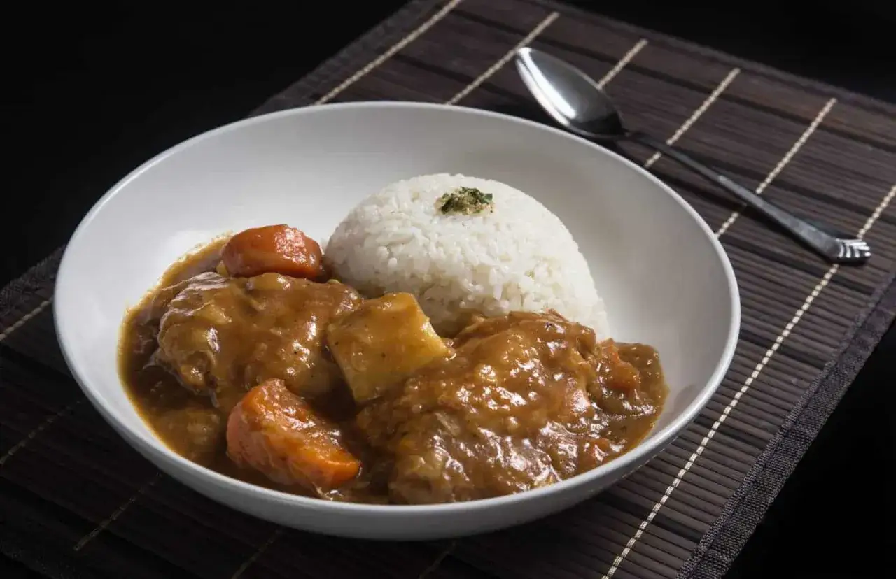 En sk&aring;l med ris och en mustig japansk curry med k&ouml;tt och mor&ouml;tter. En sked ligger bredvid.