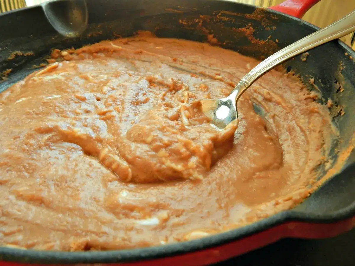 En gjutjärnspanna med krämiga refried beans, en sked vilar i den varma bönröran.