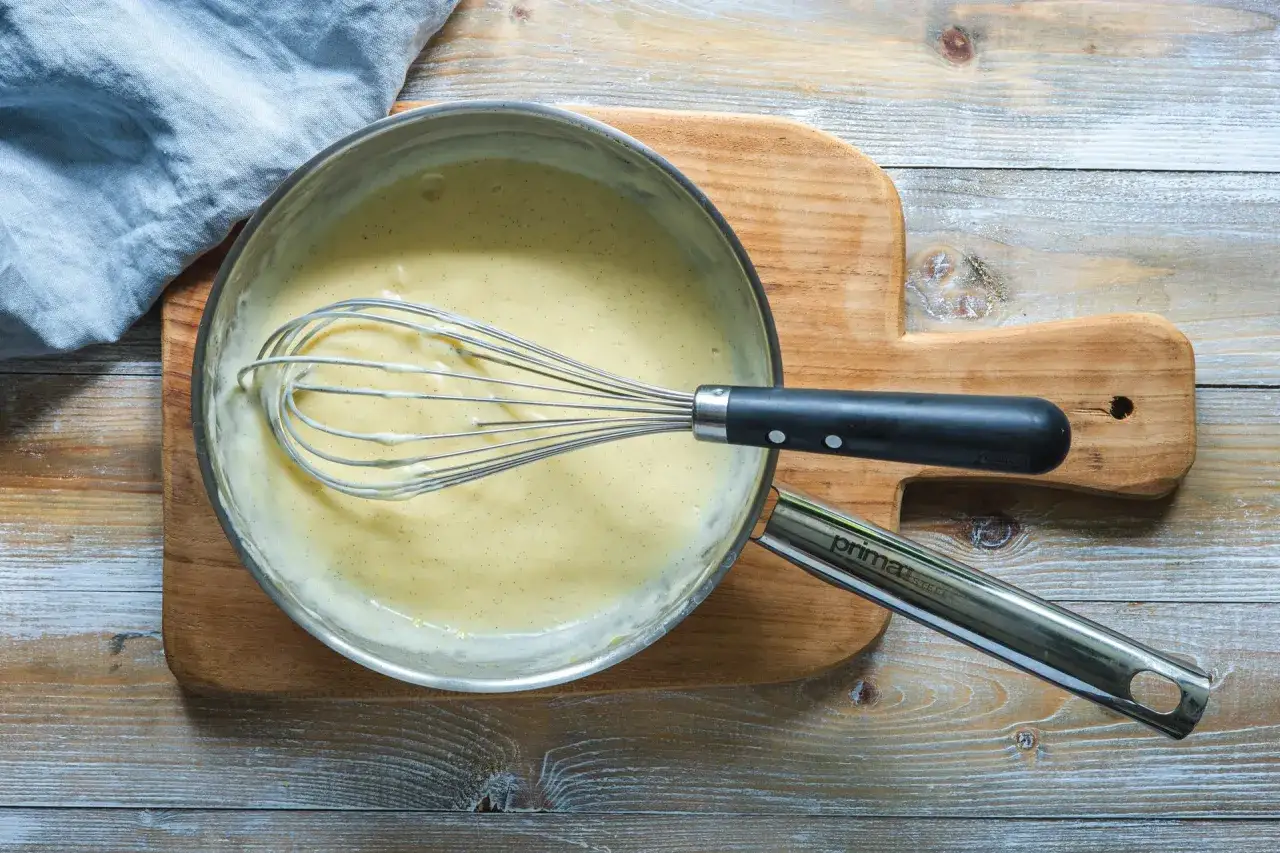 En visp r&ouml;r i en kr&auml;mig vaniljs&aring;s i en kastrull, redo f&ouml;r ett enkelt vaniljs&aring;s recept.