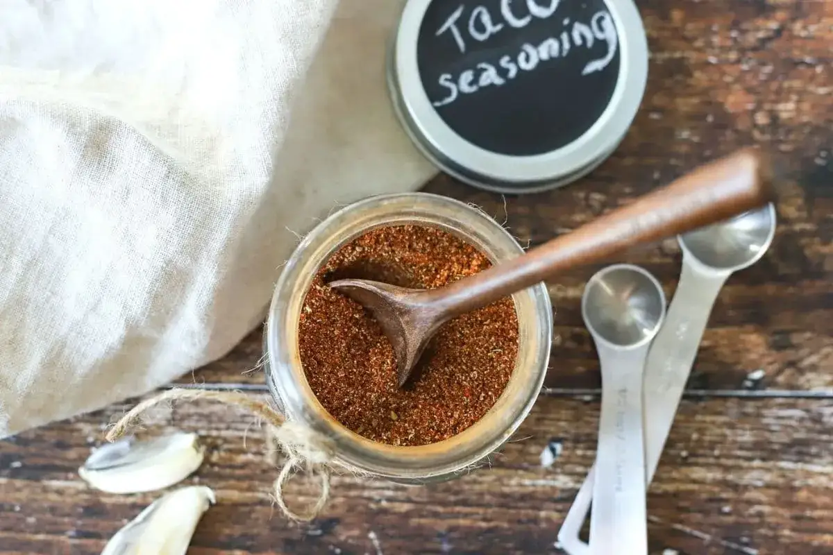 En burk med hemlagad tacokrydda, perfekt för ditt nästa tacorecept. En träsked vilar i kryddan.