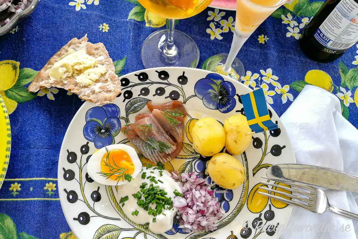 En tallrik med sill, potatis, ägg och gräddfil. En svensk flagga vajar stolt. Perfekt mat midsommar!