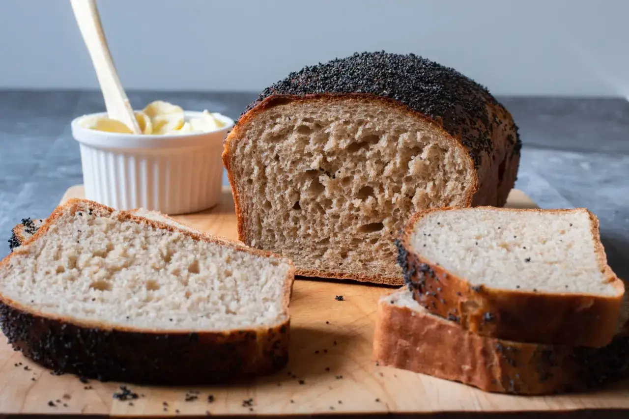 Nybakad limpa med vete och r&aring;g, toppad med vallmofr&ouml;n. Skivor ligger p&aring; en tr&auml;sk&auml;rbr&auml;da bredvid en sk&aring;l med sm&ouml;r.