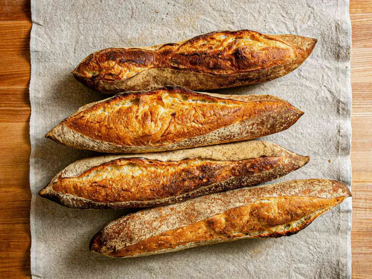 Fyra nybakade baguetter med gyllene skorpa ligger p&aring; en linneduk. Perfekt f&ouml;r ett enkelt baguette recept.