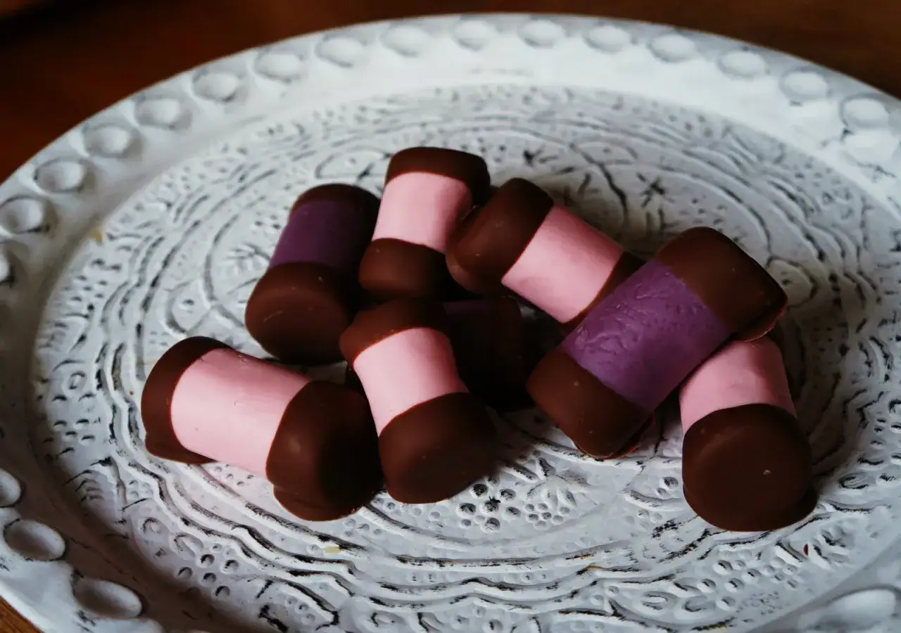 En h&ouml;g med dammsugare bakverk p&aring; en vit, m&ouml;nstrad tallrik. De &auml;r t&auml;ckta med choklad och har rosa och lila fyllning.