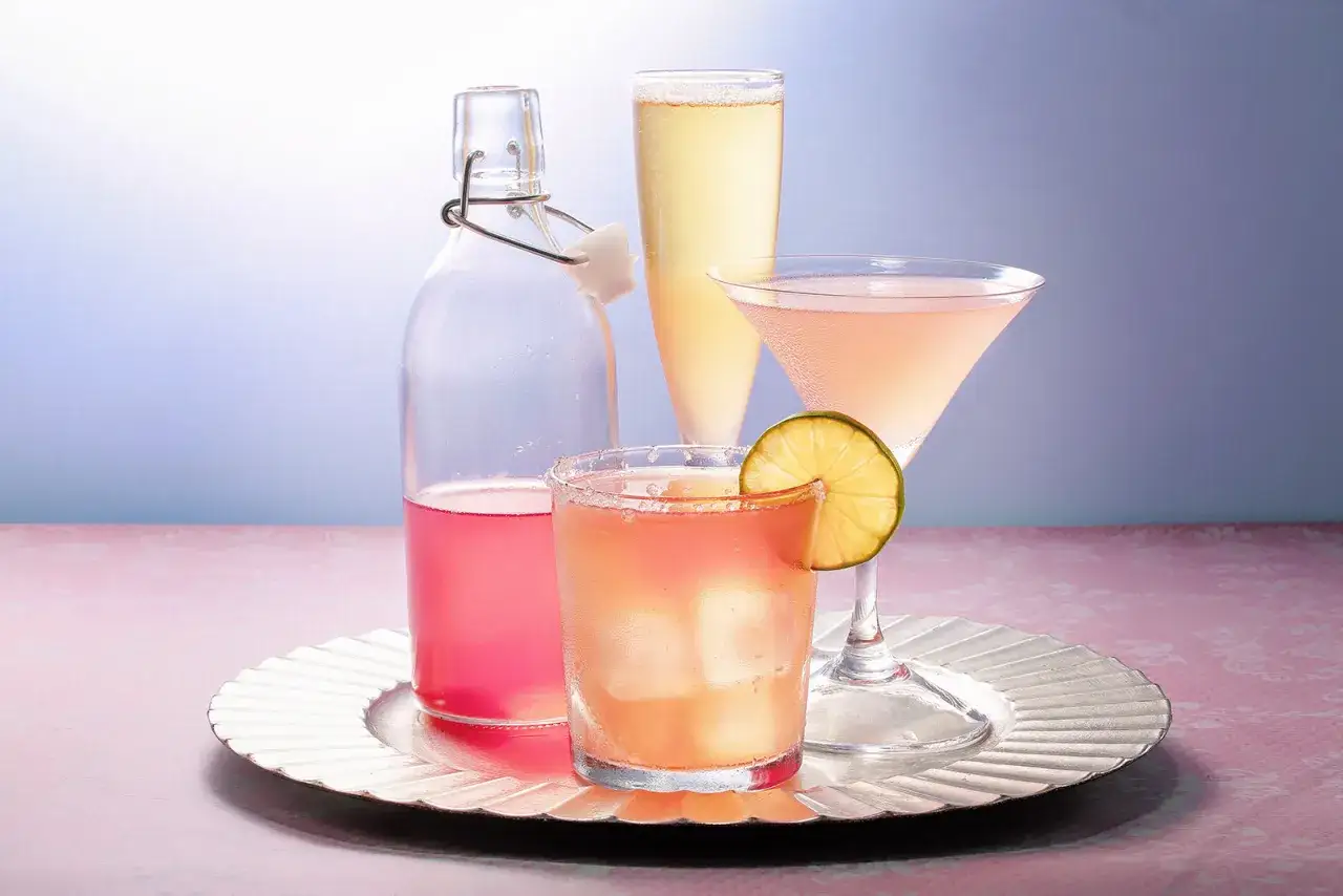 Flaska med rosa rabarbersaft, glas med is och lime, samt tv&aring; champagneglas. Ett enkelt rabarbersaft recept f&ouml;r sommaren.