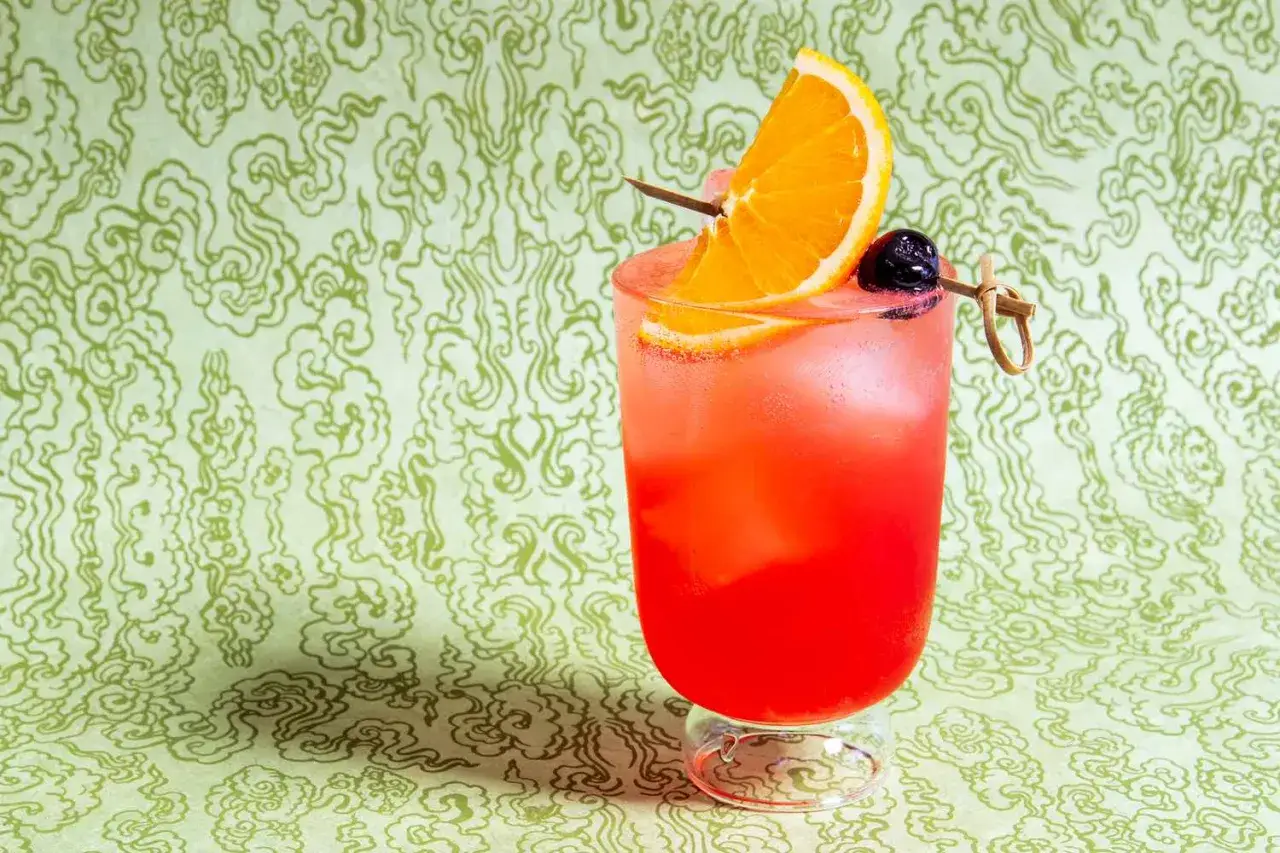 En Cointreau drink med apelsinskiva och k&ouml;rsb&auml;r, serverad med is mot en gr&ouml;nm&ouml;nstrad bakgrund.