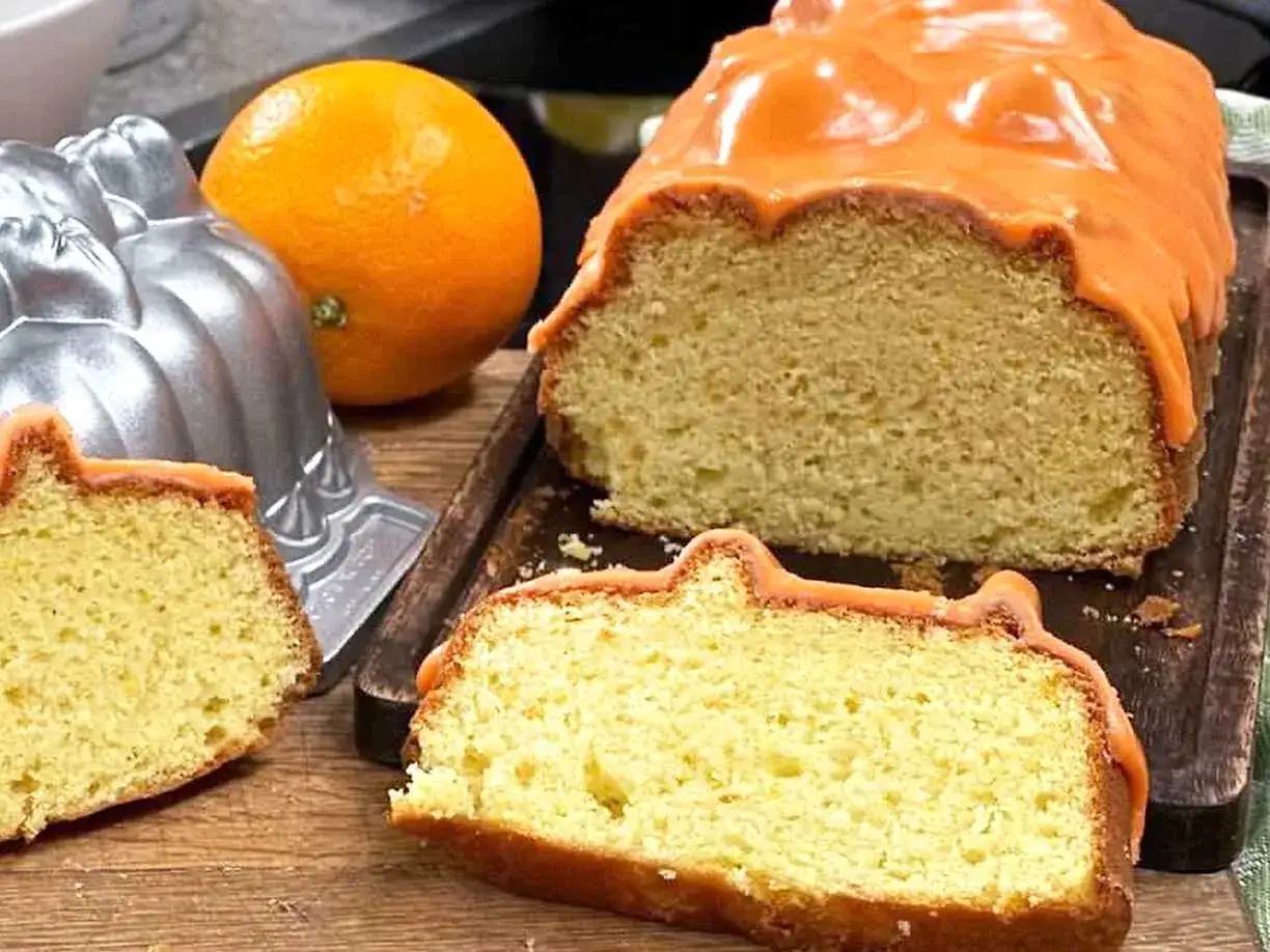 En saftig apelsin kaka med orange glasyr, en hel apelsin och en bakform.