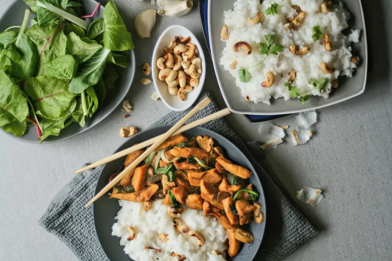 En sk&aring;l med kyckling cashew och ris, med en sidoblandning av gr&ouml;na blad och en sk&aring;l med cashewn&ouml;tter.