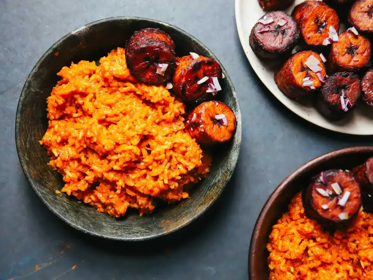 En sk&aring;l med jollof rice, toppad med friterad plantain och l&ouml;k. En annan sk&aring;l med samma r&auml;tt syns i bakgrunden.