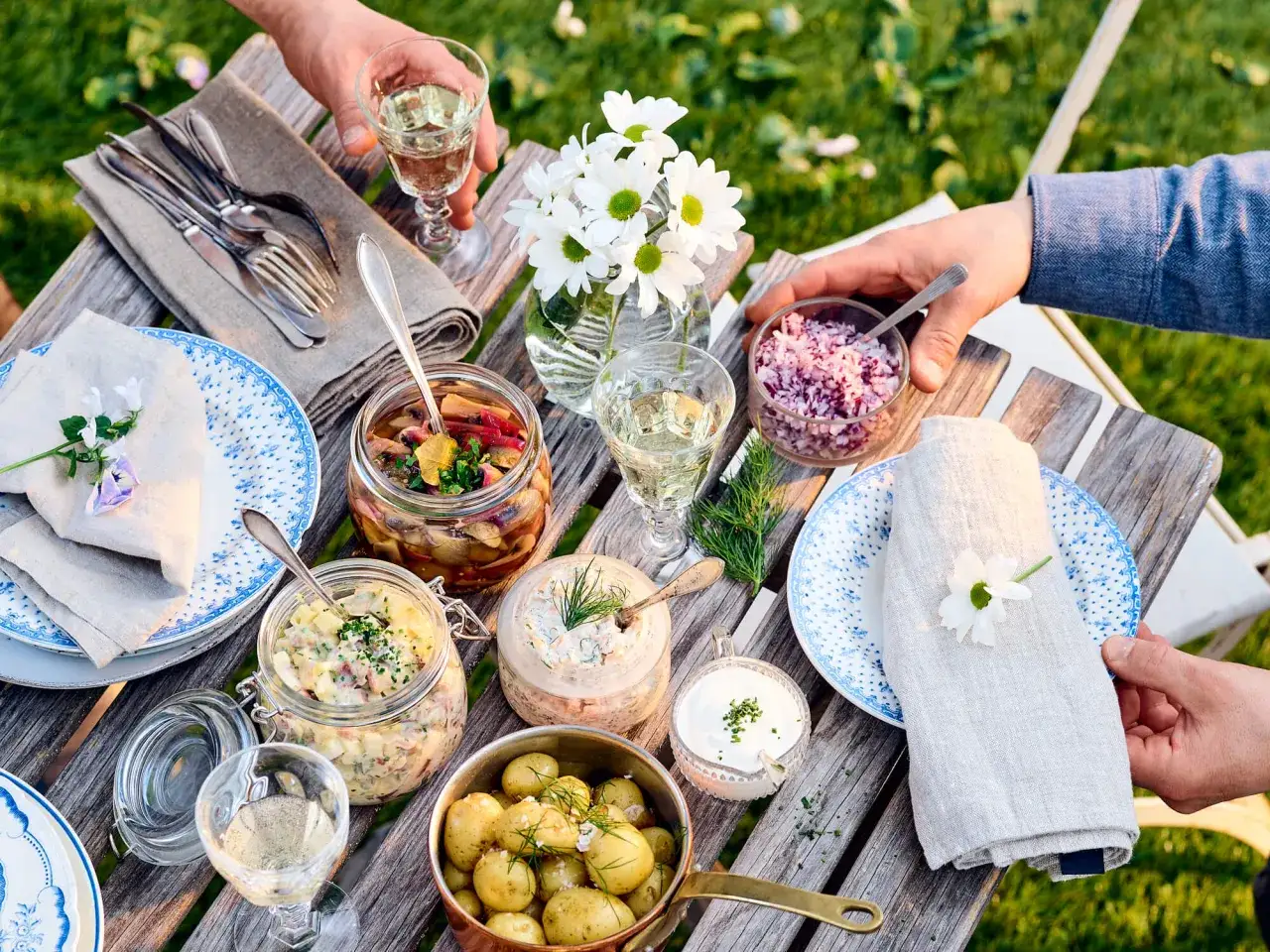 En h&auml;rlig midsommar drink p&aring; ett dukat bord med sill, potatis och blommor.