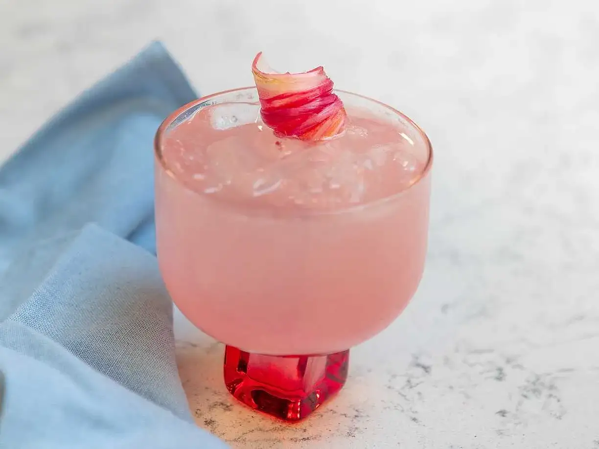 En rosa rabarber sour med is och en vacker garnering. En perfekt sommardrink.