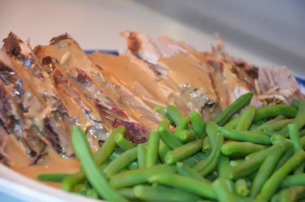 Skinkstek i gryta, saftig och uppskuren, serveras med en krämig sås och gröna bönor. En klassisk och smakrik rätt.
