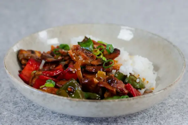 En skål med ris och en smakrik kyckling cashew-röra med paprika och svamp, toppad med salladslök.